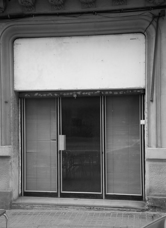 ADYTON. A project by Carlos Valverde. A black-framed glass entrance at C/ Lleida, Barcelona.